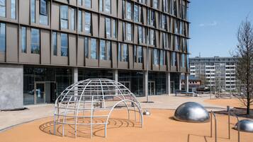 A modern building with a grid of windows and a playground area with a dome-shaped structure and metal sculptures.
