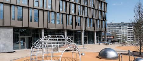 A modern building with a grid of windows and a playground area with a dome-shaped structure and metal sculptures.