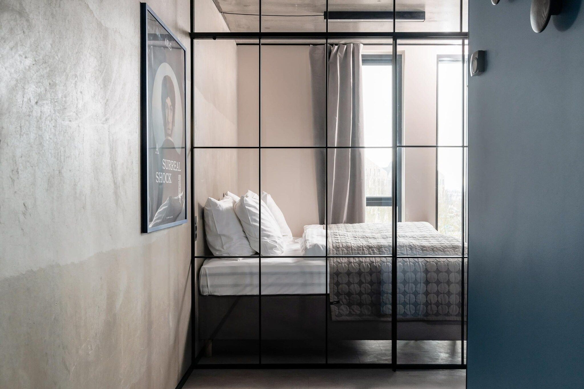 A room with a bed, a framed picture on the wall, and a window with curtains.