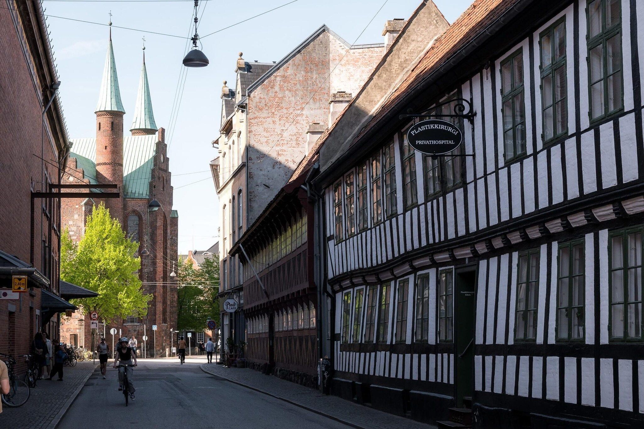 A narrow street with traditional half-timbered buildings, a church tower, and a sign for a private hospital.