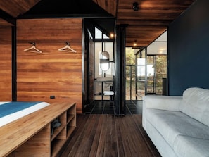Ein modernes Interieur mit Holzboden, einem Bett, einer Couch und Blick durch eine Glastür.