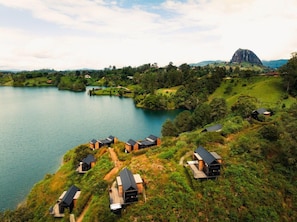 A lakeside property with multiple cabins, a prominent mountain in the background, and a clear sky. - The Boato Hotel (El Peñol)