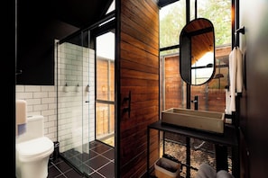 A modern bathroom with a glass shower enclosure, a wooden wall, a white sink, and a large mirror. - The Boato Hotel (El Peñol)