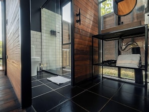 Ein modernes Badezimmer mit Duschkabine aus Glas, einer Holzwand und einem Metallregal mit Handtüchern.