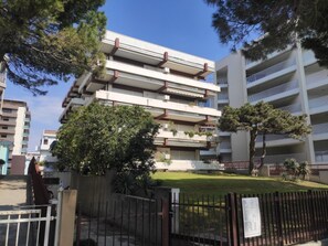 A multi-story residential building with balconies, a fenced courtyard, and surrounding trees. - Seafront Apartment by the City Centre (Lignano Sabbiadoro)