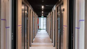 Un long couloir bordé de portes de part et d’autre, qui mène à une sortie lumineuse au bout.