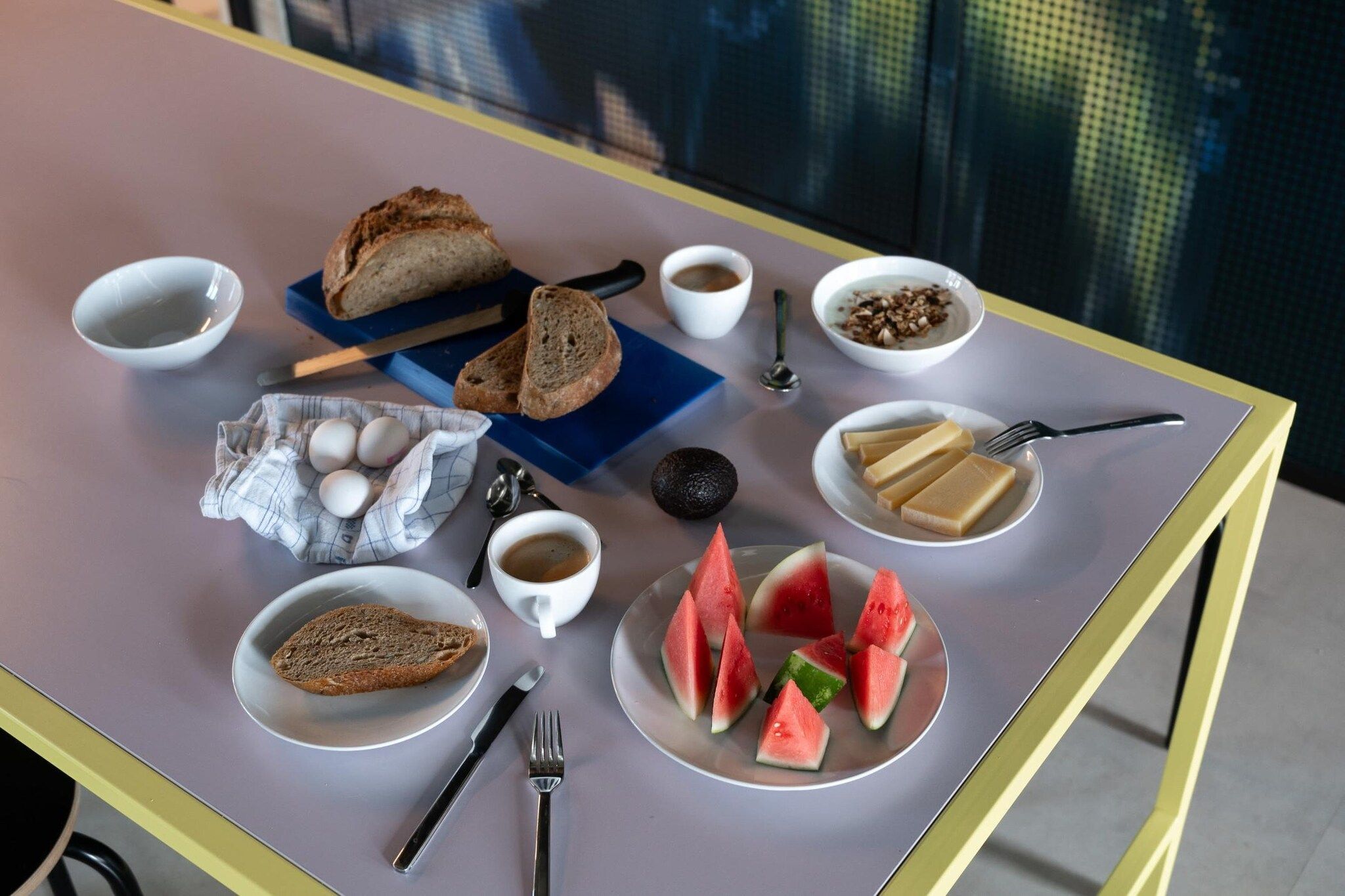 Una tavola imbandita per la colazione, con pane, uova, caffè e fette di anguria.