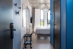 Ein Hotelzimmer mit einem Bett, einem Schreibtisch mit Stuhl, einer Schreibtischlampe, einem Telefon und einem Fenster mit Vorhängen.
