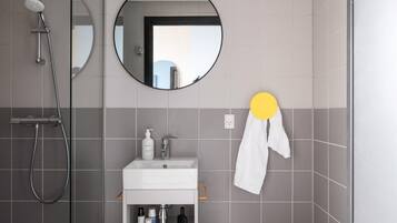 Une salle de bain moderne équipée d’une douche, d’un lavabo avec des articles de toilette et d’un miroir.