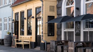 Une rue bordée d’un immeuble doté de grandes fenêtres, d’un banc en bois et d’un espace extérieur aménagé avec des parasols.
