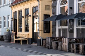 Een straat met een gebouw, grote ramen, een houten bank en terras met parasols.