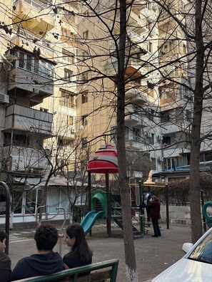 Ein Spielplatz mit Rutsche und Klettergerüsten, umgeben von Bäumen und einem mehrstöckigen Gebäude.