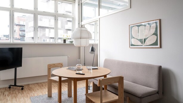 Ein modernes Wohnzimmer mit einem runden Holztisch, zwei Stühlen, einem grauen Sofa, einer Stehlampe und einem gerahmten abstrakten Gemälde an der Wand.