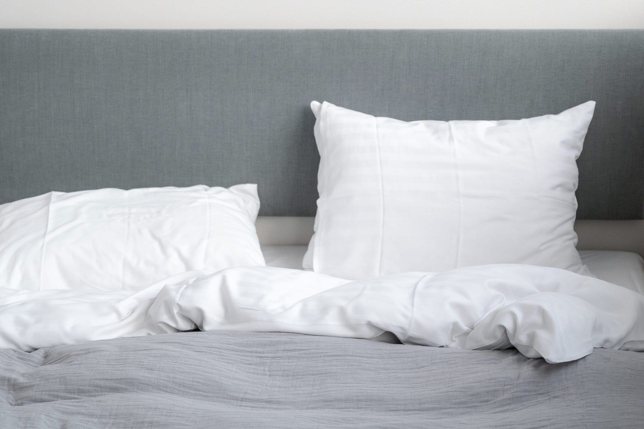Ein Bett mit weißer Bettwäsche und einem grauen Kopfteil.