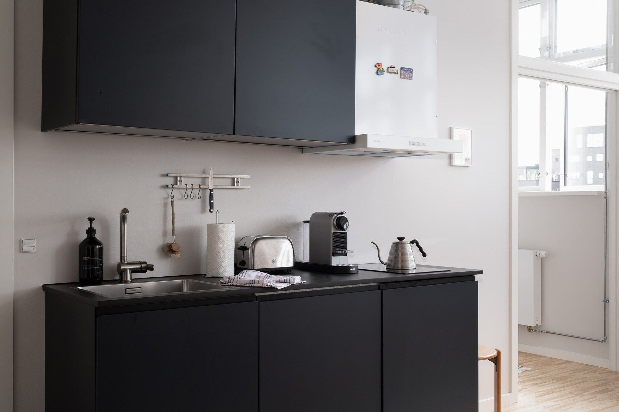 A modern kitchen with a black countertop, a kettle, a coffee maker, and a hanging knife rack.