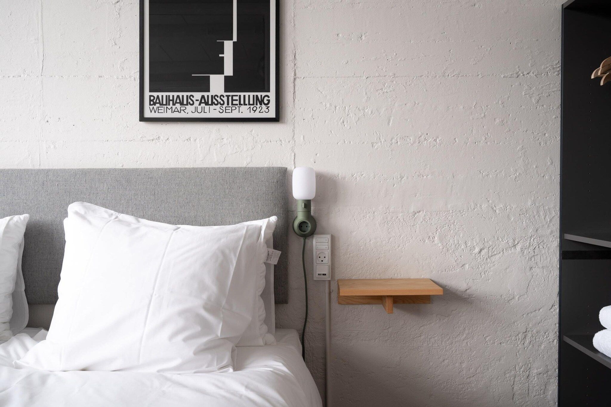 Et soveværelse med seng, lampe på væggen og et billede i ramme.