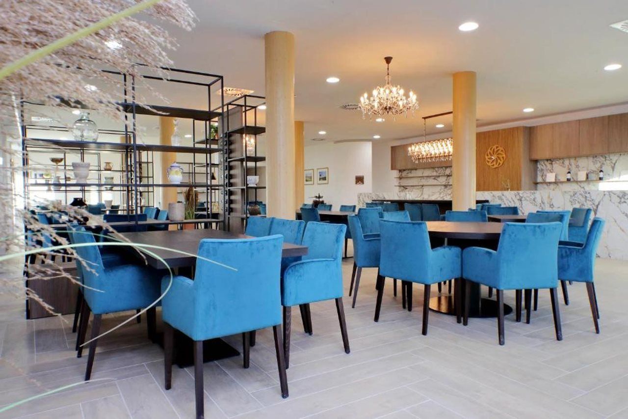 Un'area pranzo moderna con sedie imbottite blu e un tavolo centrale, circondata da una scaffalatura in metallo con oggetti decorativi.