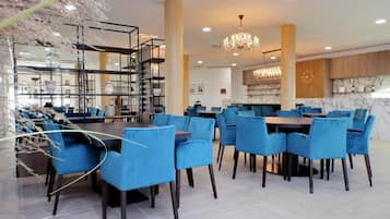 Un'area pranzo moderna con sedie imbottite blu e un tavolo centrale, circondata da una scaffalatura in metallo con oggetti decorativi.