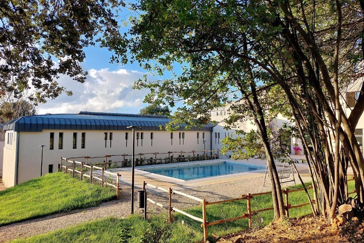 Un edificio con piscina, circondato da una recinzione in legno e alberi.