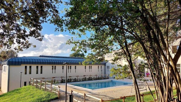 Un edificio con piscina, rodeado por una valla de madera y árboles.