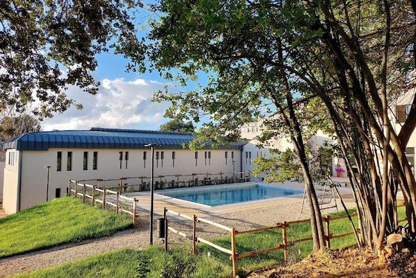 Un edificio con piscina, rodeado por una valla de madera y árboles.