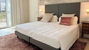 Un dormitorio con una cama grande, dos mesitas de noche, un cabecero y vistas al exterior.