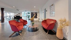 Un vestíbulo moderno con sillones rojos, un piano de cola y una estantería.