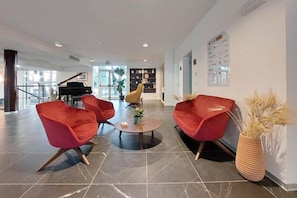 Un vestíbulo moderno con sillones rojos, un piano de cola y una estantería.