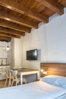 A bedroom with a wooden ceiling, a bed, a desk with chairs, a television, and a pendant light.