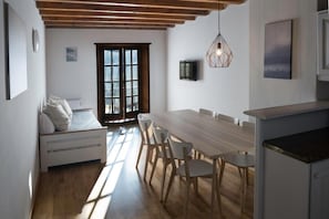 Un interior moderno con una mesa de comedor de madera, sillas blancas, una cama con vistas y una lámpara colgante.