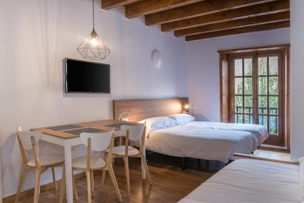 Un dormitorio con cama, escritorio con sillas, televisor y ventana con vistas.