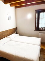 Un dormitorio con dos camas, cabecero de madera, una ventana con cortinas florales y un radiador.