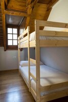 A room with two bunk beds, wooden ceiling beams, a window, and a white wall.