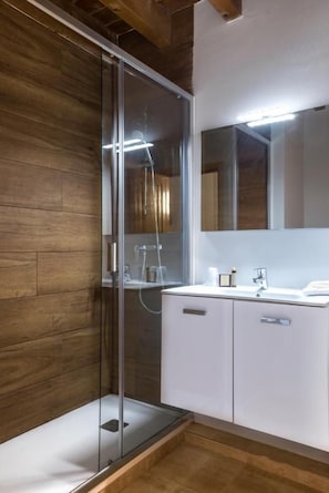 Un baño moderno con cabina de ducha de vidrio, paneles de madera en la pared y un tocador blanco con espejo.