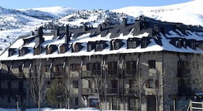 Un edificio de varios pisos con balcones, rodeado de colinas nevadas.