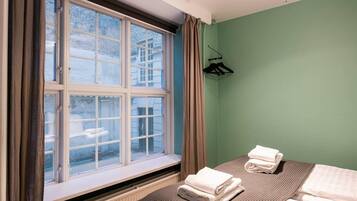 Ett hotellrum med ett stort fönster, en säng med två kuddar, ett element och en klädställning.
