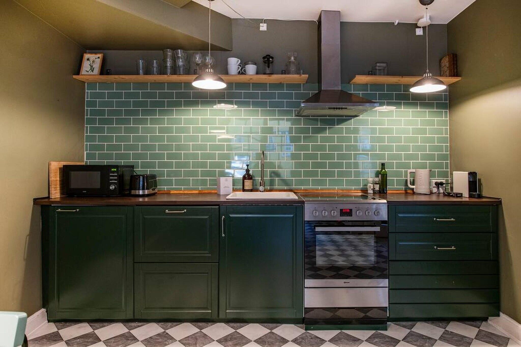 A kitchen with green cabinets, a microwave, a stove, and two hanging pendant lights.