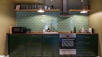 A kitchen with green cabinets, a microwave, a stove, and two hanging pendant lights.