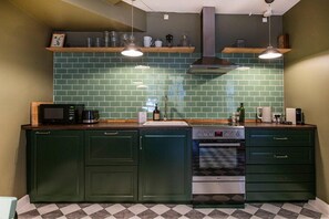 A kitchen with green cabinets, a microwave, a stove, and two hanging pendant lights. - Home Near Buses and Metro (København)