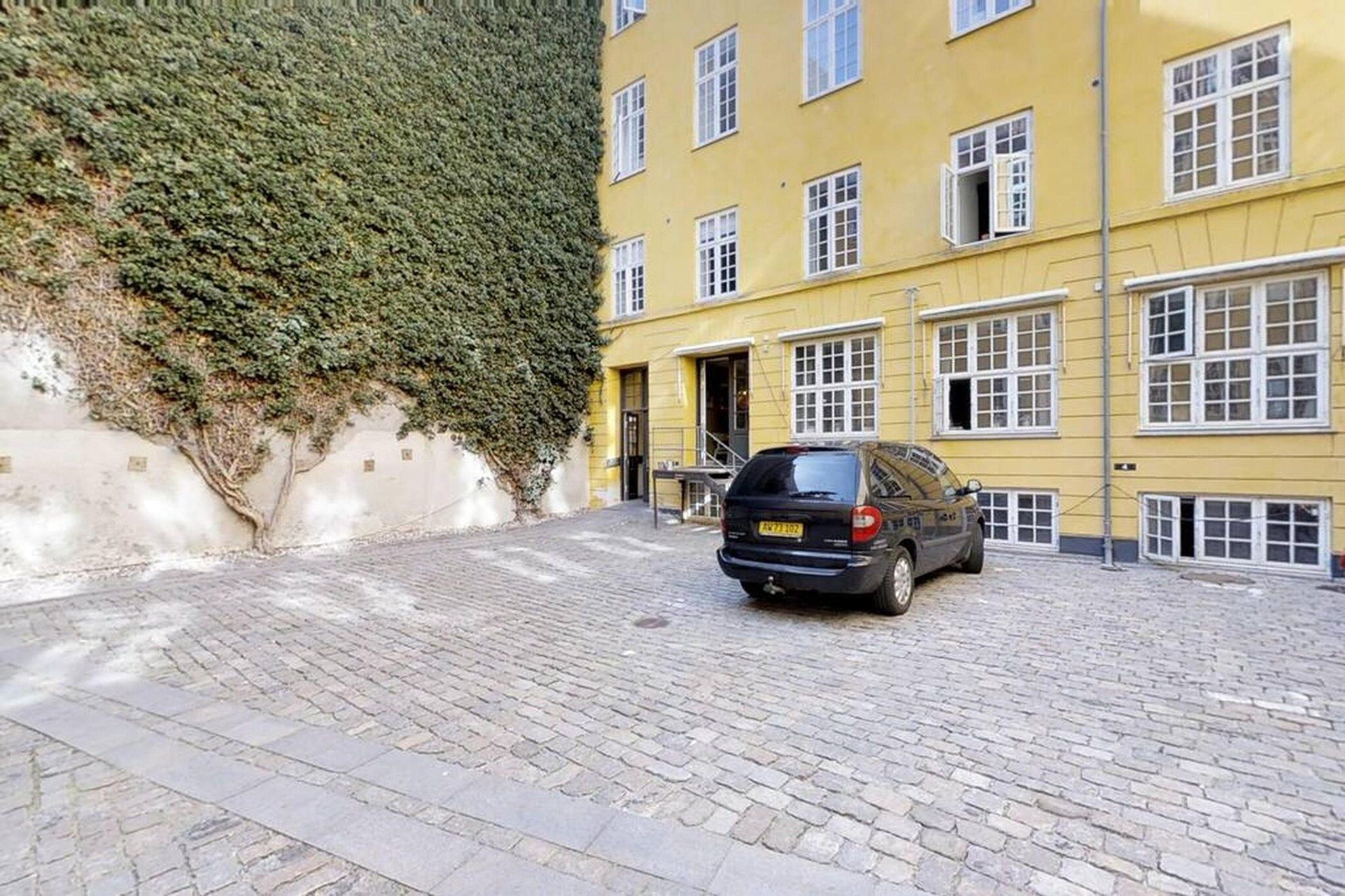 A car parked on a cobblestone street in front of a yellow building with multiple windows.