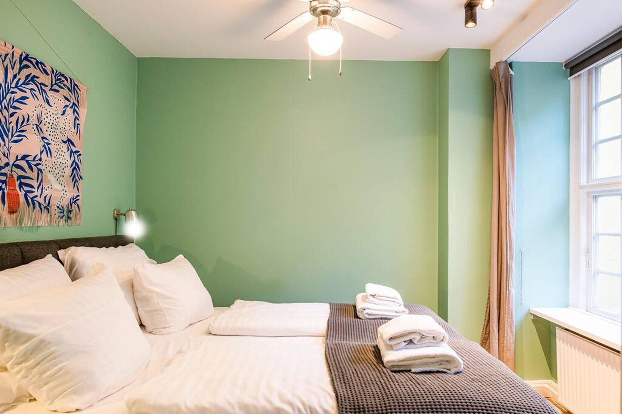 A hotel room with a bed, pillows, a folded towel, a ceiling fan, and a window with curtains.