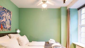 A hotel room with a bed, pillows, a folded towel, a ceiling fan, and a window with curtains.