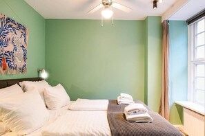 A hotel room with a bed, pillows, a folded towel, a ceiling fan, and a window with curtains. - Home Near Buses and Metro (København)