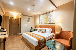 Ein Hotelzimmer mit Bett, Schreibtisch, Stuhl, Tisch, Deckenventilator und einem Bild an der Wand.