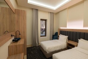 A hotel room with two beds, a desk, a chair, and a window with curtains. - Maskan Alolya (Al Khobar)