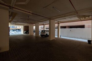 An indoor parking garage with concrete pillars, a tiled floor, and a white vehicle parked in the distance. - Maskan Alolya (Al Khobar)