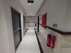 A hallway with a fire extinguisher mounted on the wall, a fire alarm, and a door at the end. - Maskan Alolya (Al Khobar)