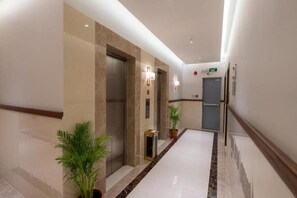 Pasillo de hotel con ascensores, plantas en macetas y un piso de baldosas limpias.