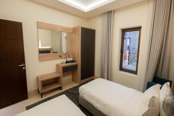 Habitación de hotel con cama, escritorio con espejo, armario y ventana con cortinas.