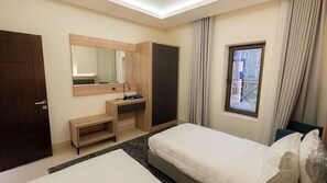 A hotel room with a bed, a desk, a mirror, a wardrobe, and a window with curtains. - Maskan Alolya (Al Khobar)